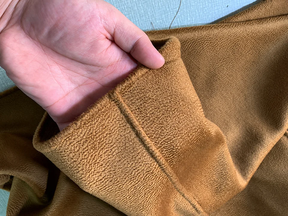 A hand opening a brown fabric seam to show the folded edge and joining line