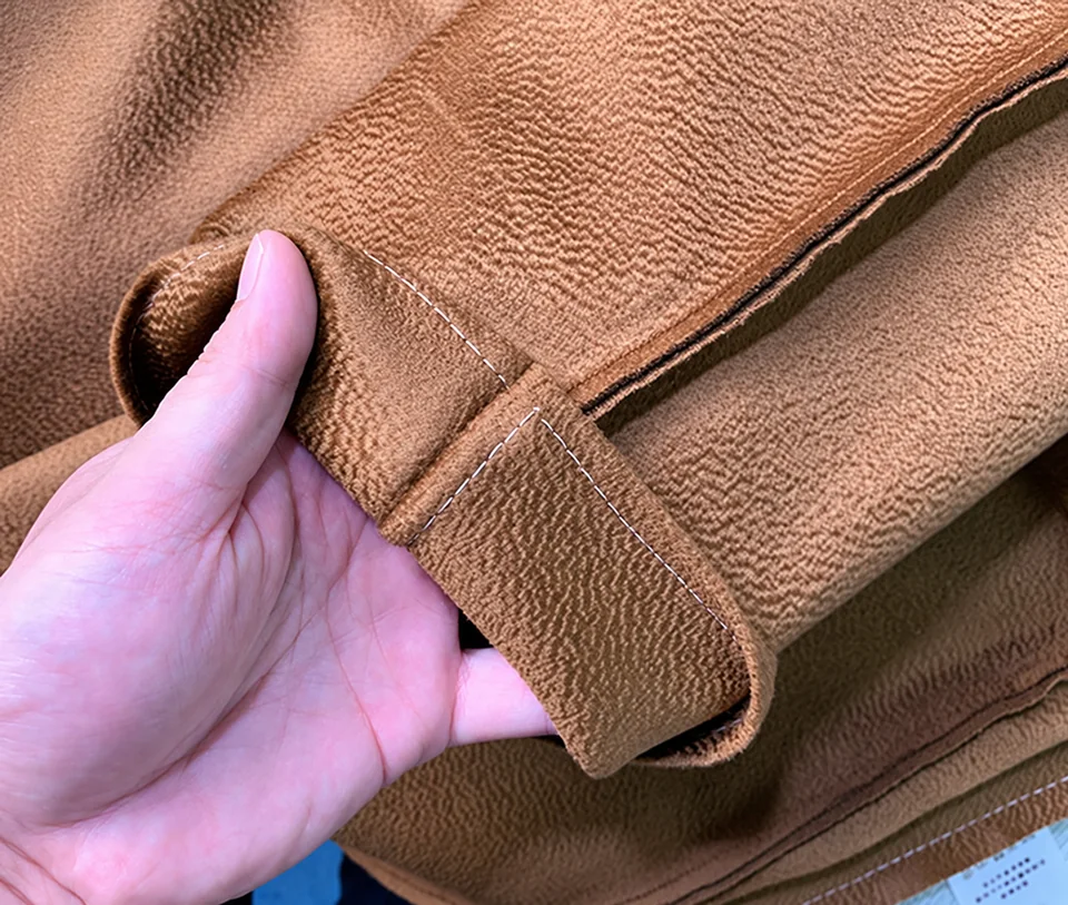 A hand showing a strap-like fabric detail beside an inside seam with white preparation stitches
