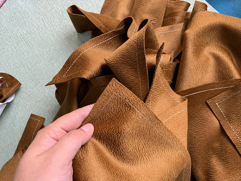 Brown cut fabric panels on a work surface, with one piece held by hand
