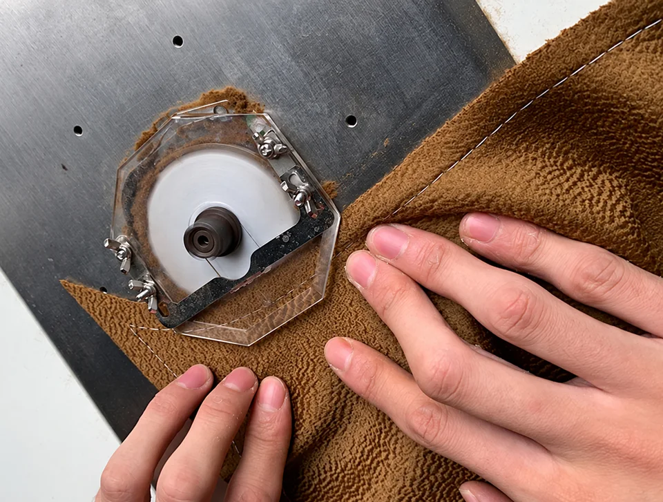 Hands guiding the edge of brown fabric beside a small circular seam-splitting tool