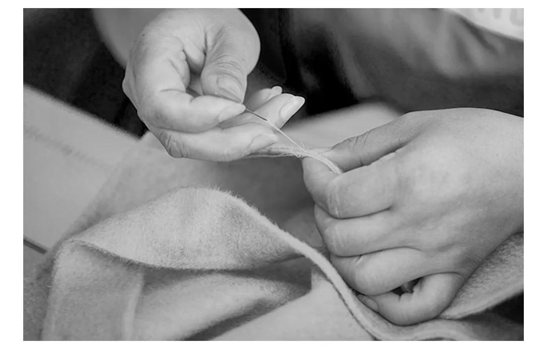 Hands carefully stitching the edge of a garment in a TINGSU craft photograph