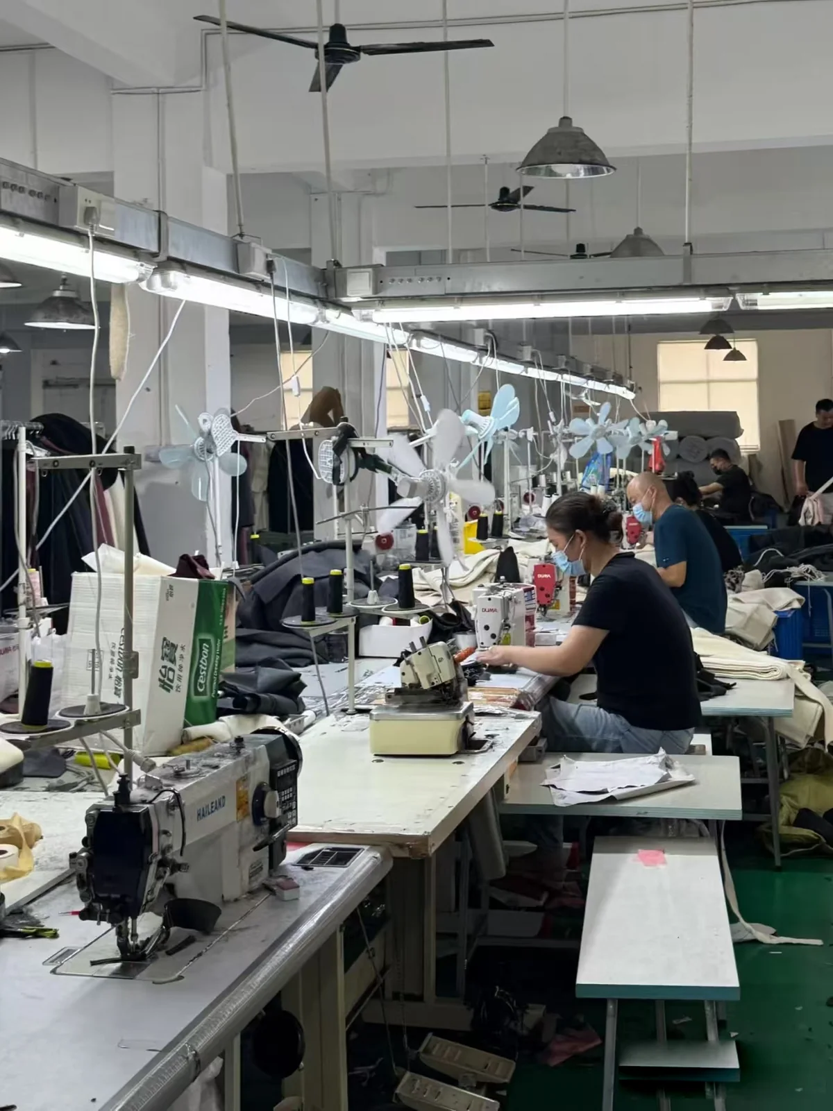 A real TINGSU production photograph showing garments being sewn at a row of worktables
