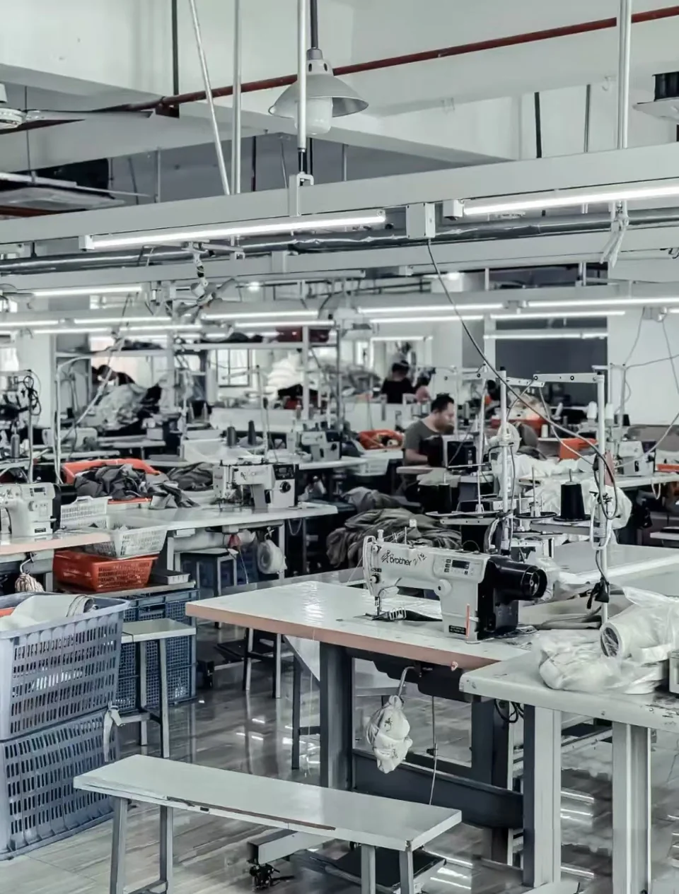 Rows of sewing stations, garment pieces and overhead lighting in a workshop